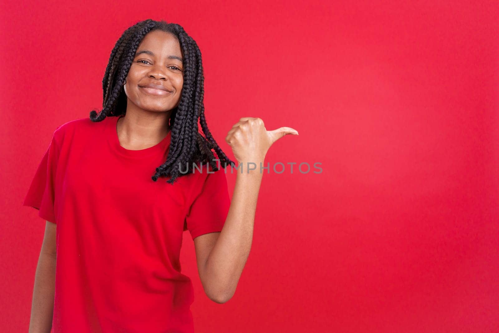 Happy african woman pointing a blank space to the side in studio with red background