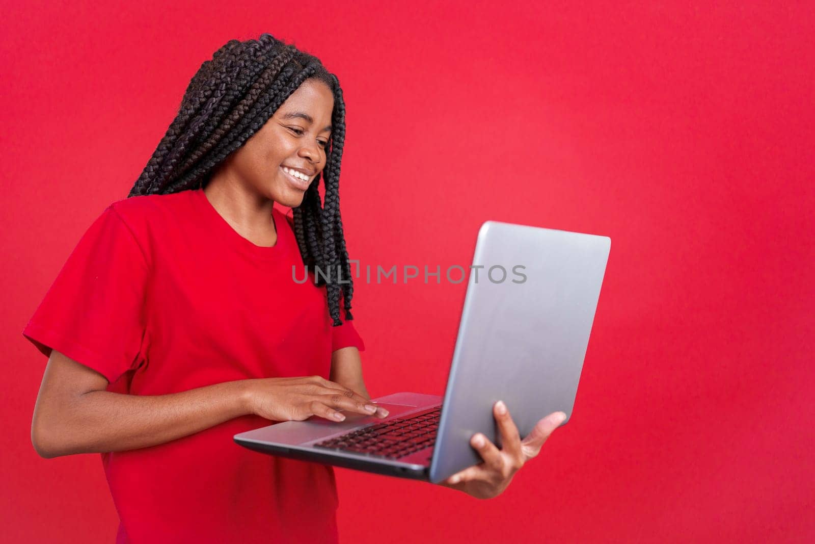 African woman smiling while using a laptop in studio with red background