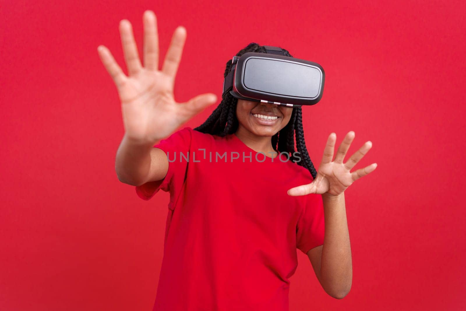 Happy african woman with Virtual Reality goggles in studio with red background