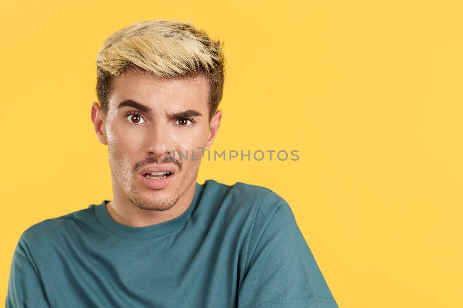 Gay man looking at the camera with a blank look on his face in studio with yellow background