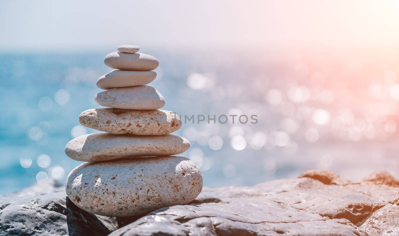 Pyramid stones on the seashore with warm sunset on the sea background. Happy holidays. Pebble beach, calm sea, travel destination. Concept of happy vacation on the sea, meditation, spa, calmness.