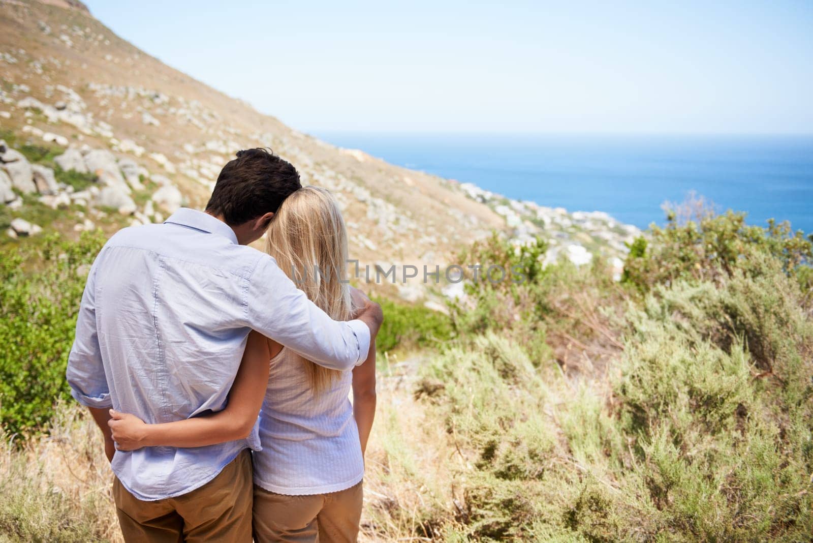 Romance with a view. Rear view of a happy young couple embracing as they enjoy the view from the mountainside