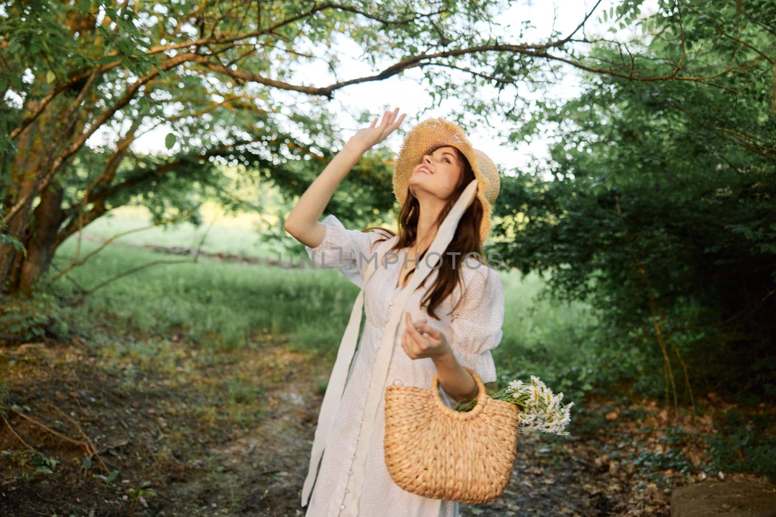 happy, smiling woman in a wicker hat with a basket of daisies in her hands walks through the forest by Vichizh
