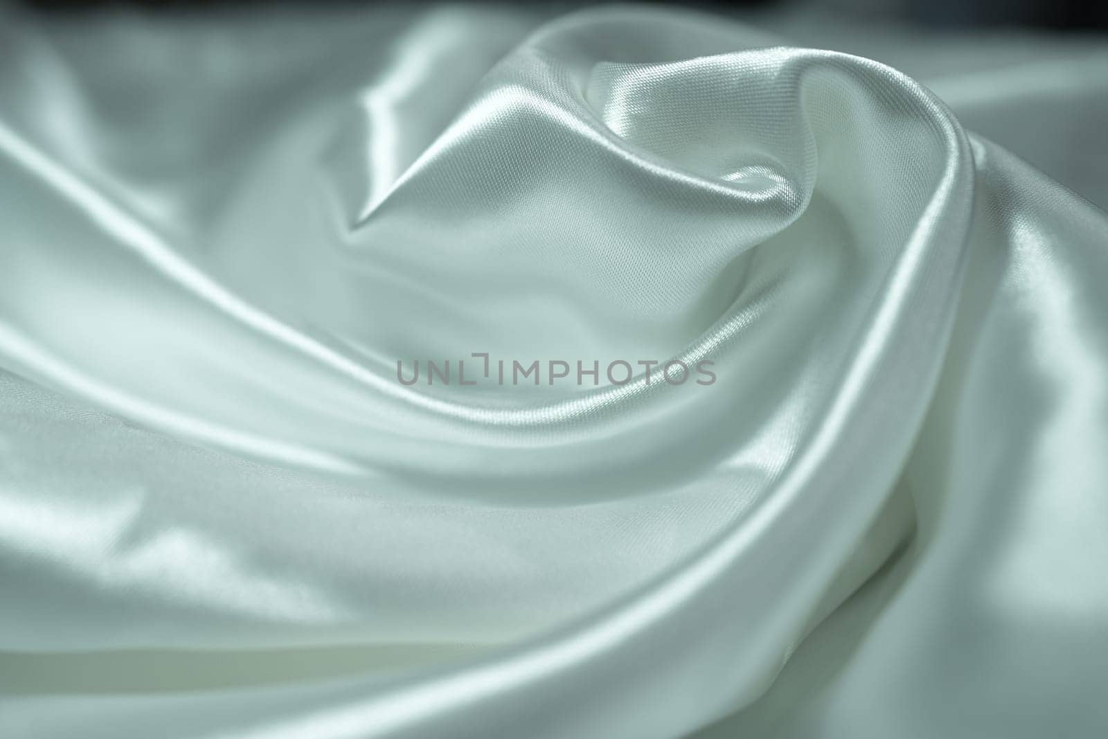 White satin fabric background with wavy soft folds for selling product. White Texture - light Wavy Glossy Silk Drapery. Shiny smooth fabric. Elegant background for design.