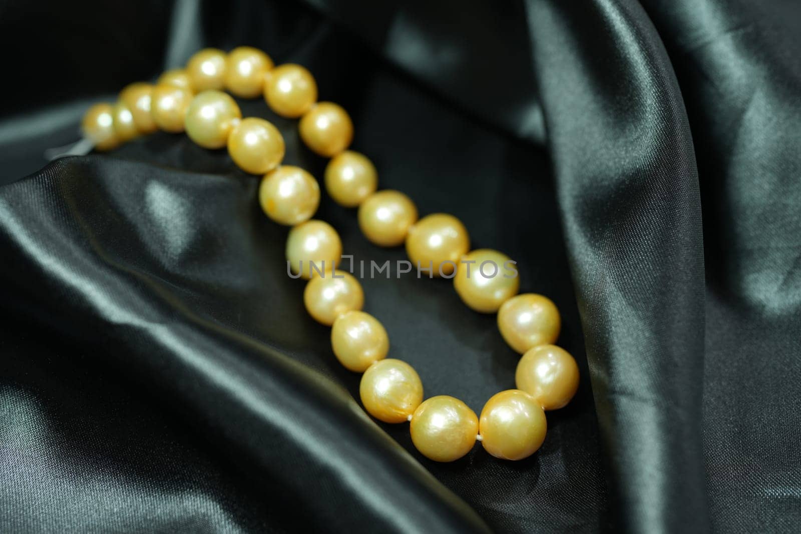 Golden Pearl necklace on black satin background by nantachai