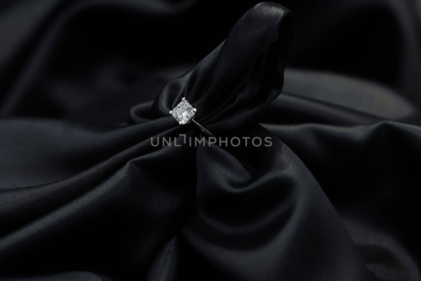 Fine jewelry as diamond ring in white gold or platinum setting with black satin fabric background. Jewelry shop concept for luxury store. engagement ring foe wedding couple lover