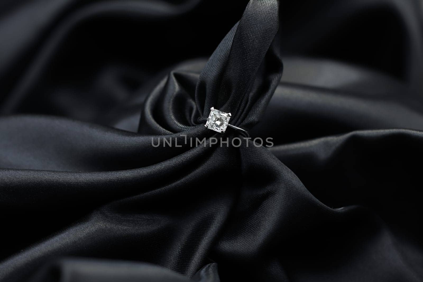 Fine jewelry as diamond ring in white gold or platinum setting with black satin fabric background. Jewelry shop concept for luxury store. engagement ring foe wedding couple lover
