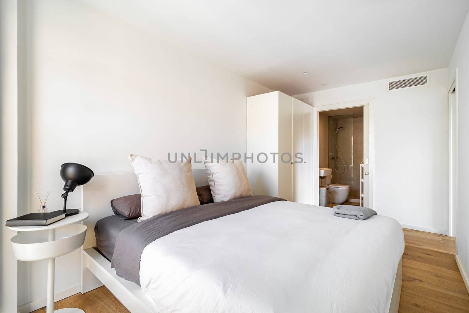 Bright bedroom with cozy bed, big pillows, wardrobe and bathroom. Interior of modern apartment in European city