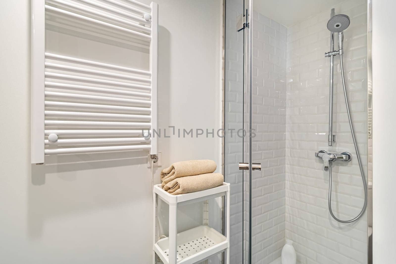 Interior of white bathroom in refurbished apartment. Shower zone with heater, sink and mirror.