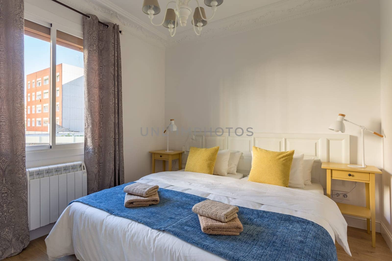 Interior of touristic bedroom with window. Yellow pillows on bed with towels. An apartment ready for booking by tourists by apavlin