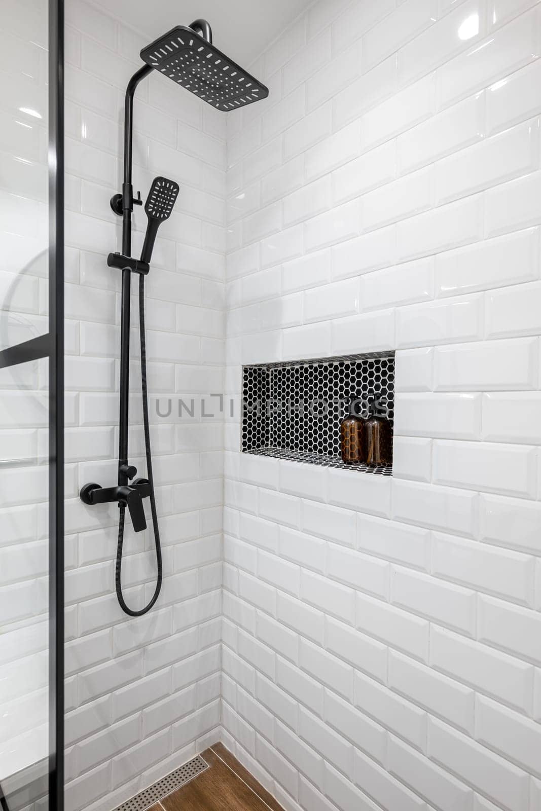 New black shower head on holder in white tiled bathroom in modern apartment