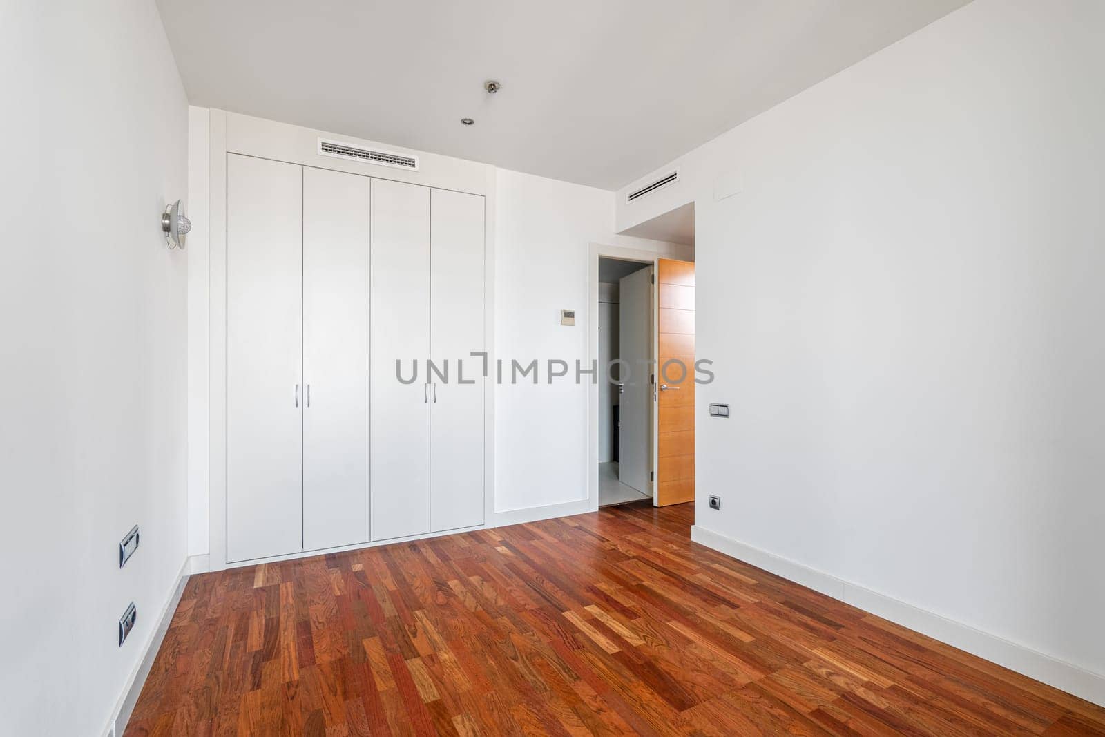 Interior of empty apartment, white room with built-in wardrobe and parquet floor.