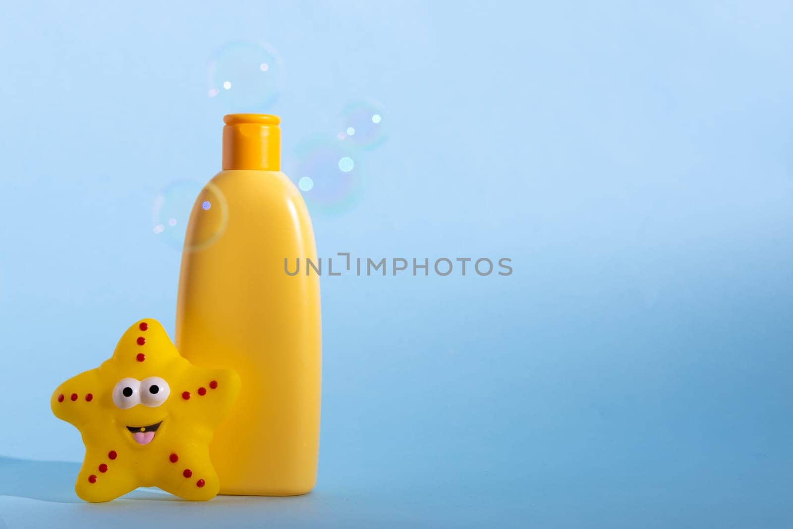 Yellow plastic bottle with baby cosmetic and funny bath toy. Soap bubbles on a background. The concept of children's bath time