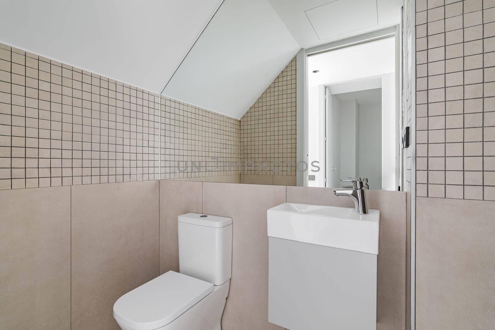 Interior of modern bathroom with beige tiles, toilet and small sink.