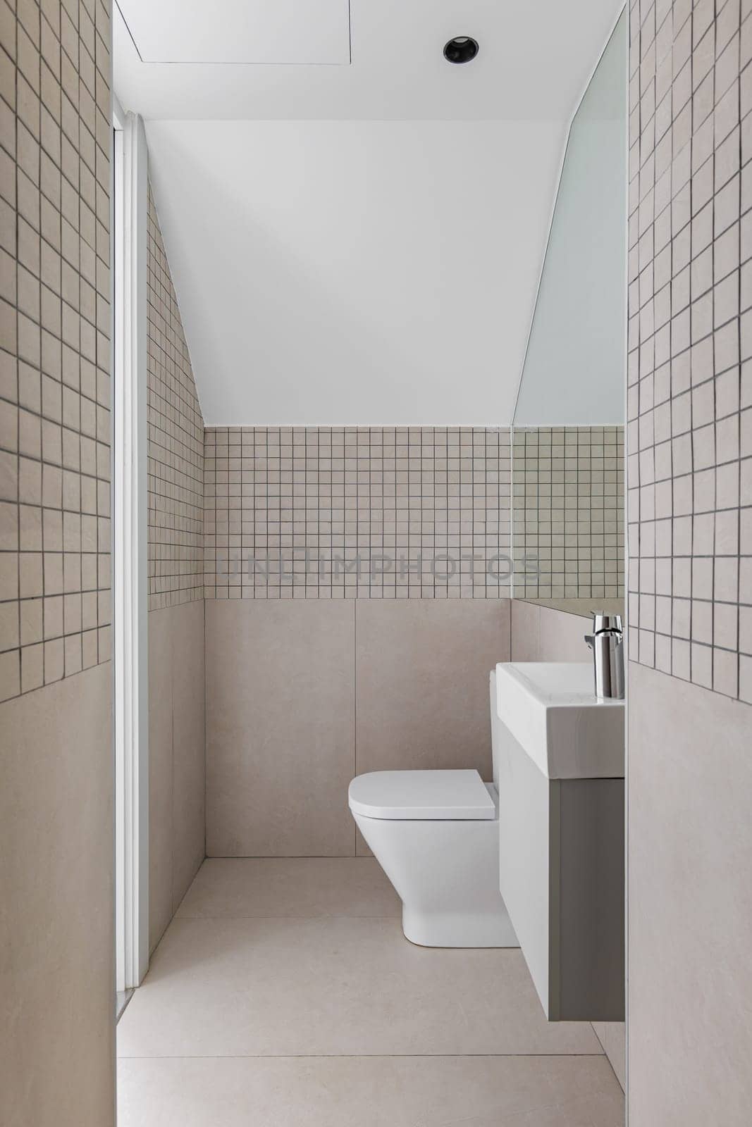 Interior of narrow bathroom with small sink and toilet. View from the shower zone of modern bathroom with beige tiles by apavlin