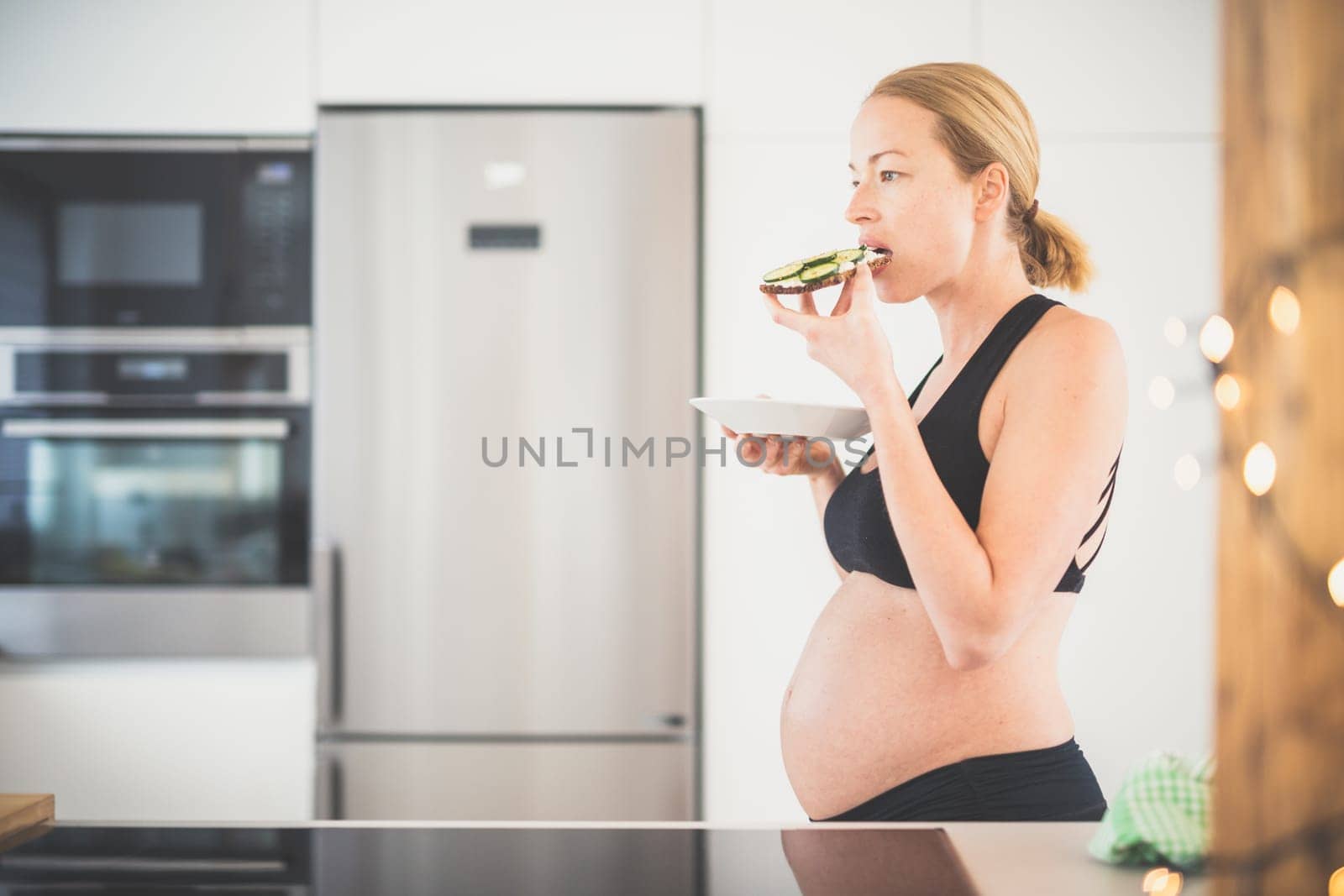 Beautiful sporty fit young pregnant woman having a healthy snack in home kitchen. Healty lifestyle concept