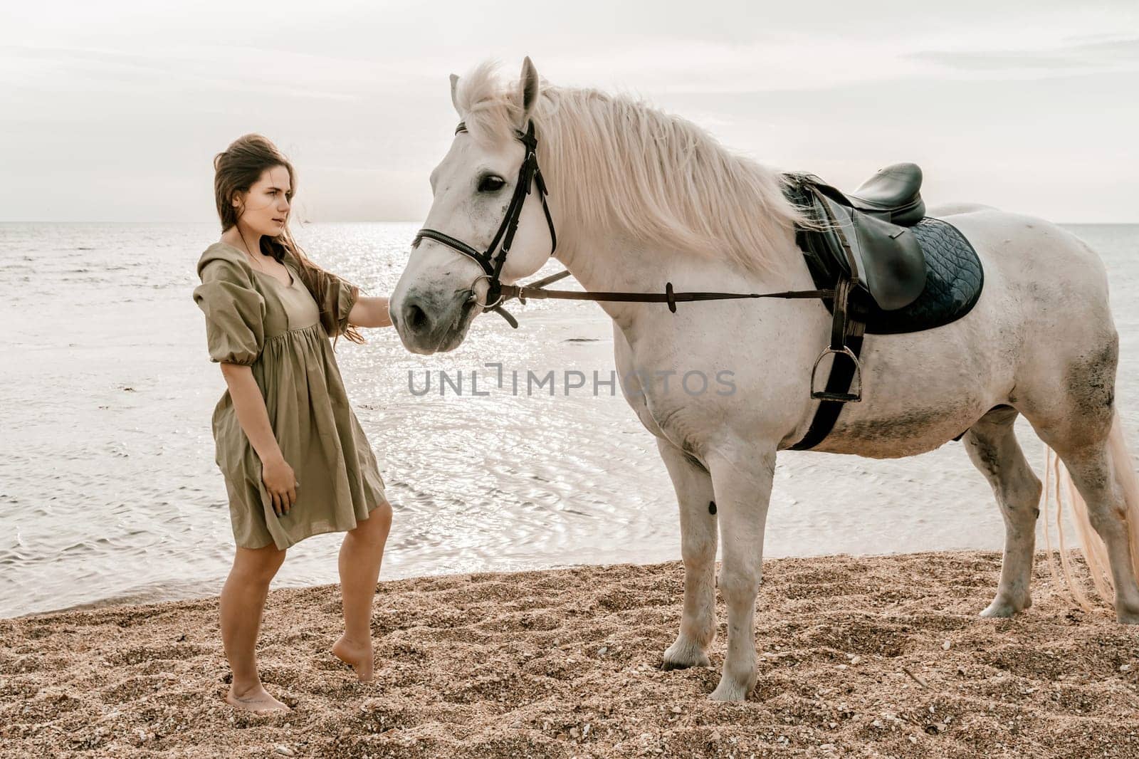 A white horse and a woman in a dress stand on a beach, with the sky and sea creating a picturesque backdrop for the scene