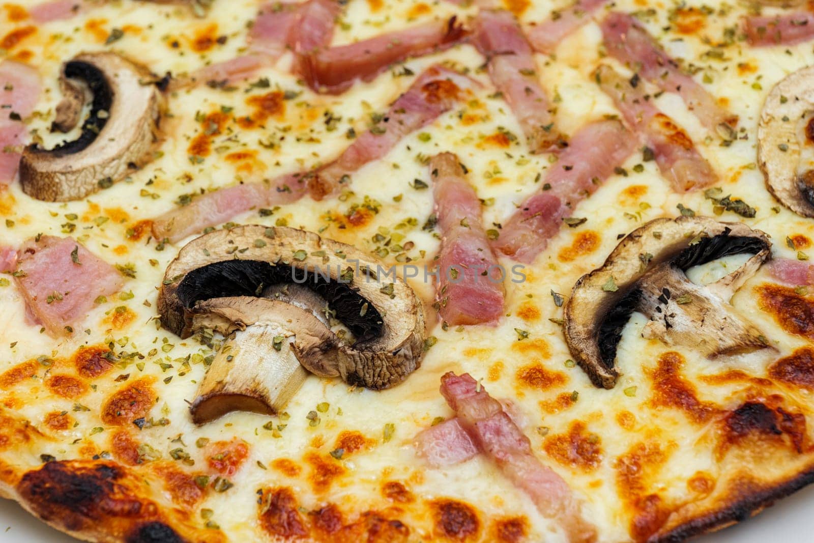 Close-up of pizza topped with mushrooms, ham, cheese and oregano. Selective focus.