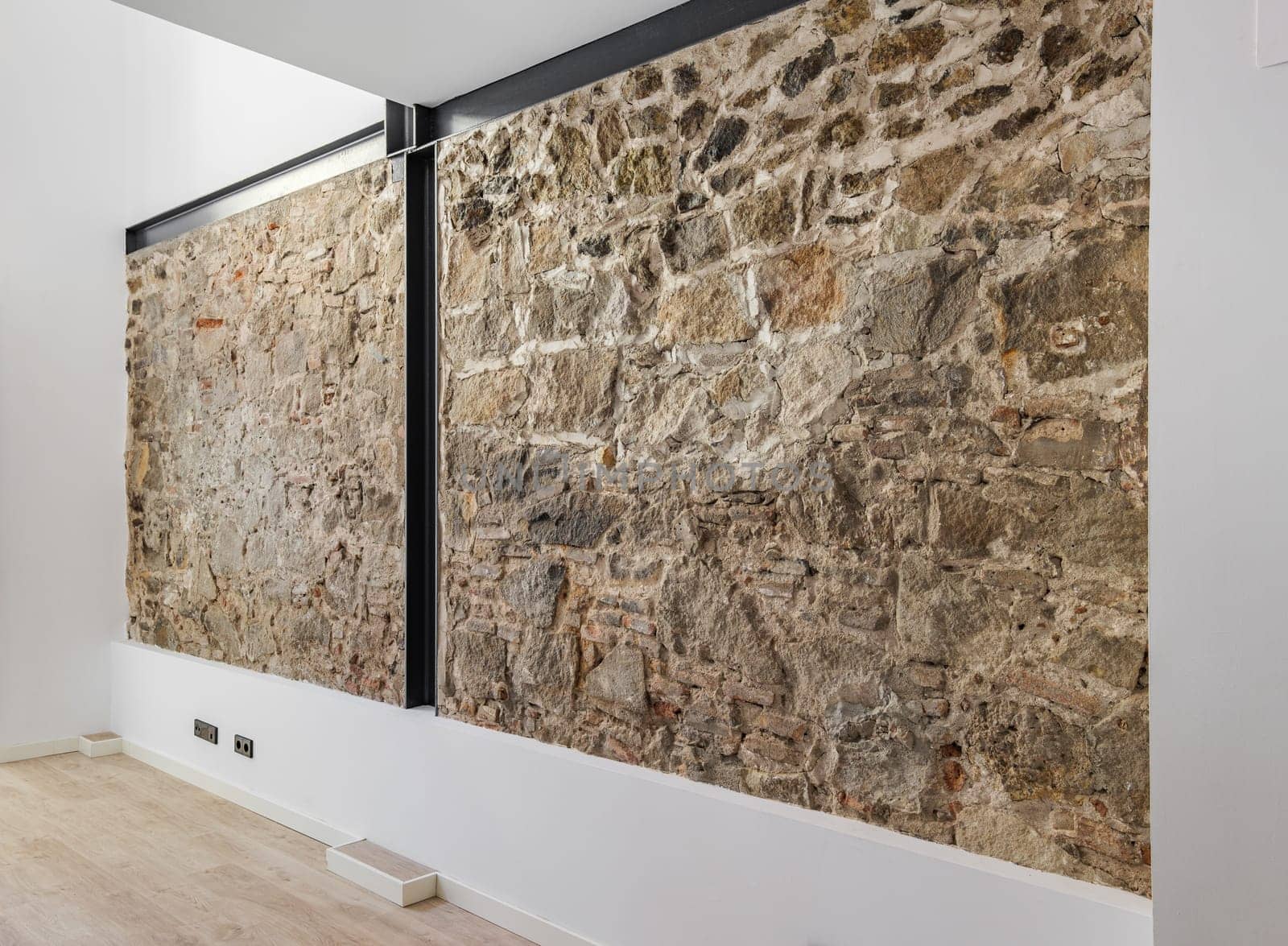 Restored ancient wall left from old city buildings in Barcelona. Interior of empty renovated apartment with stone wall