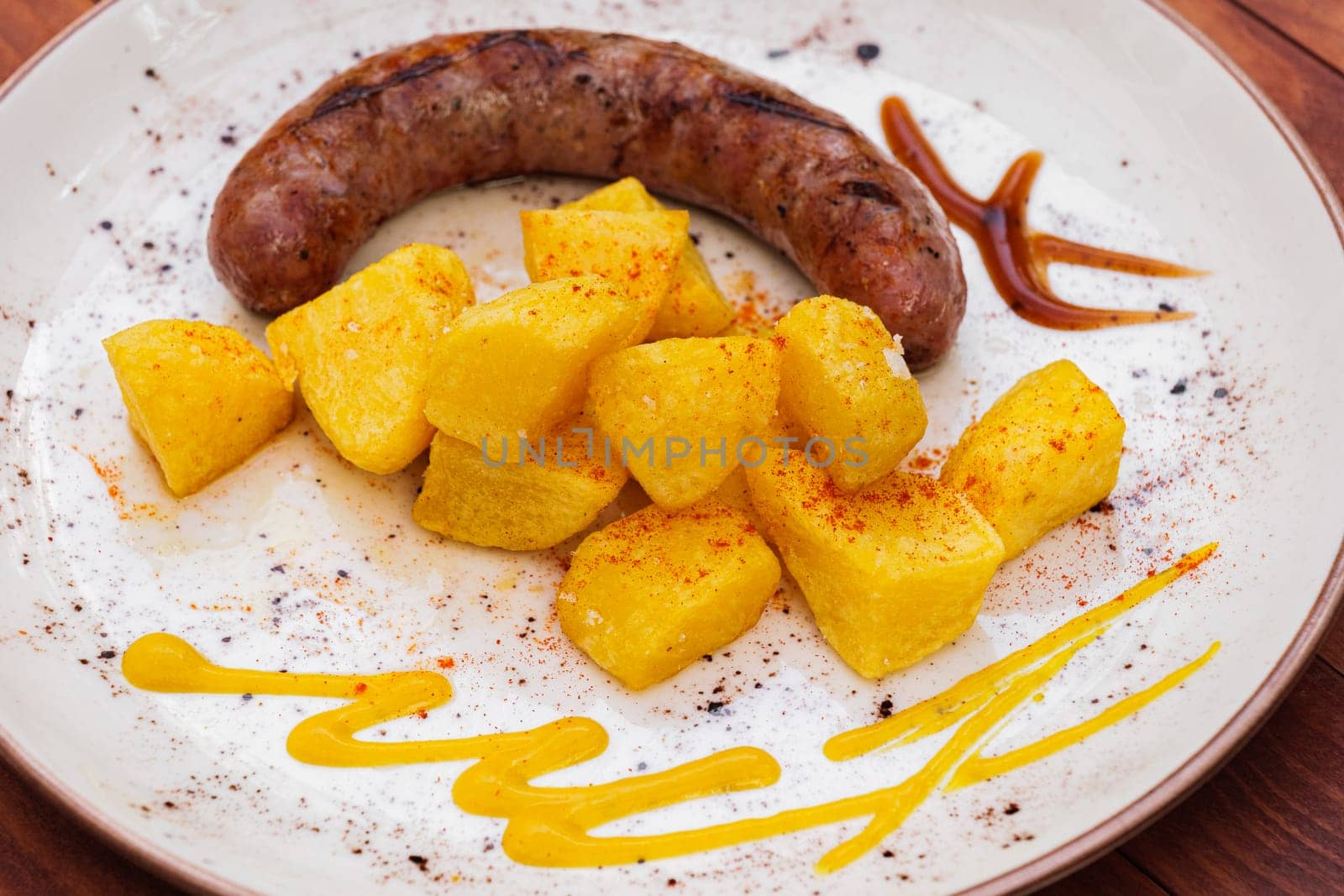 Fried potatoes and treditional spanish pork sausage butifarra with sauces on white plate. by apavlin