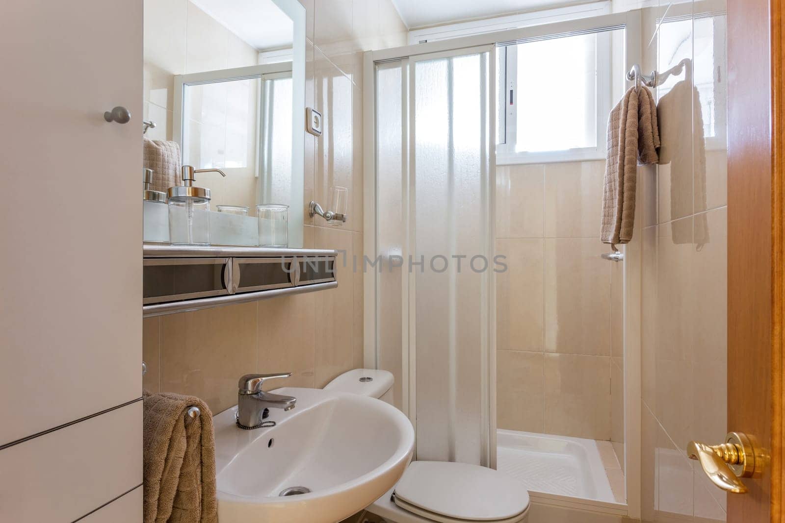 Simple style interior of small restroom with beige ceramic tile walls, white sink, classic WC toilet and shower cabin