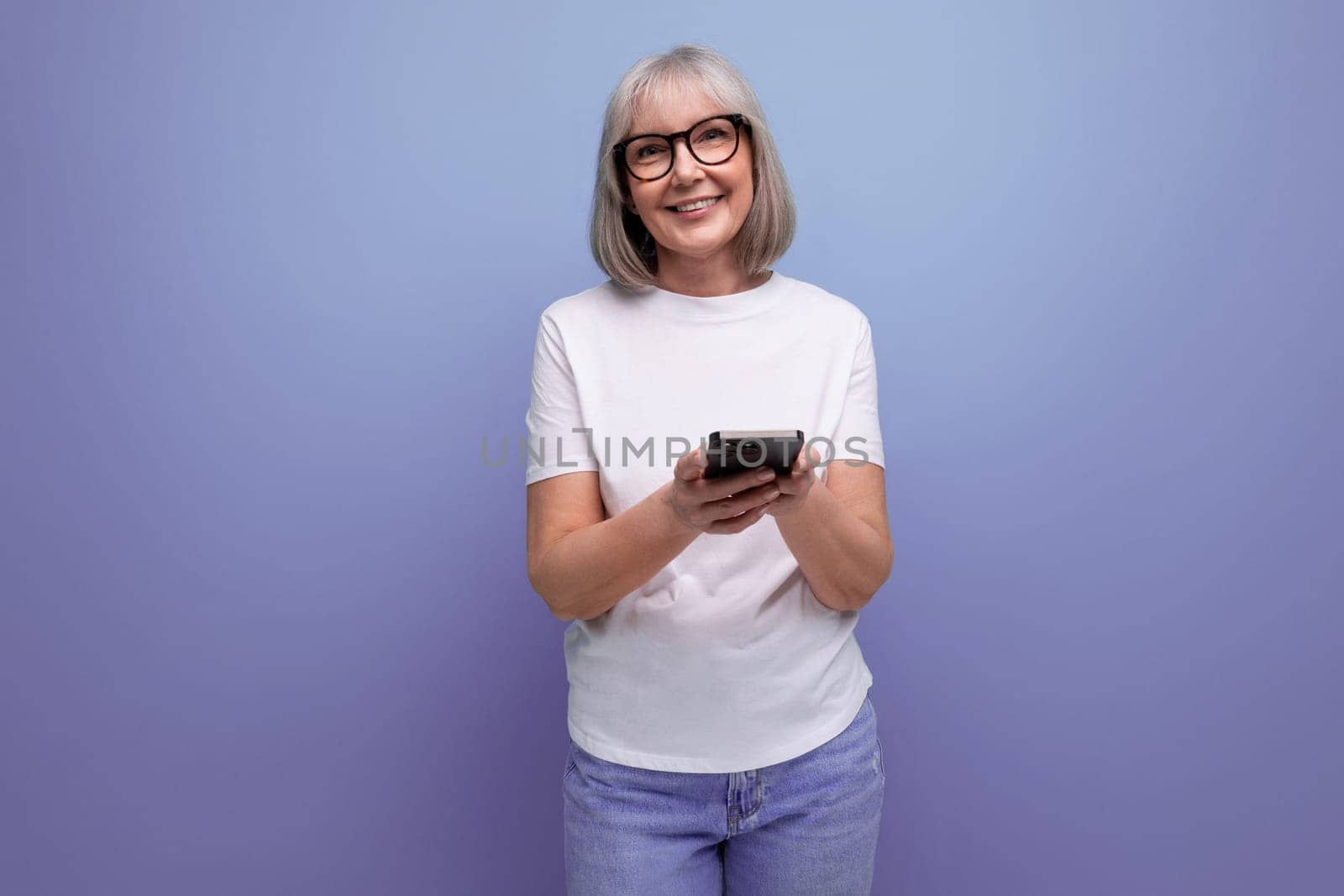 smiling gray-haired mature woman chatting on the internet in a smartphone on a bright studio background.