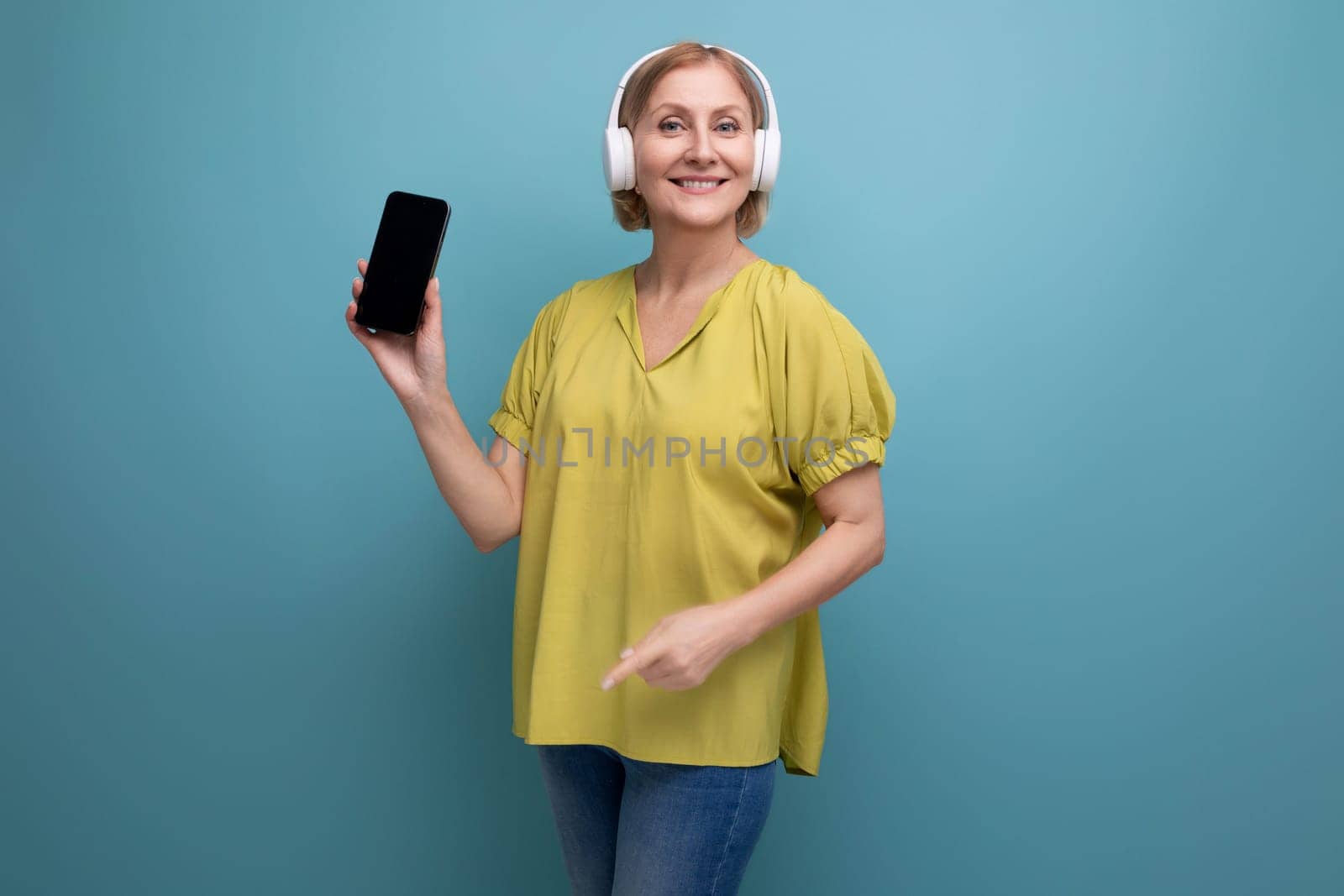 middle aged business. blond woman with headphones and a smartphone in her hands by TRMK