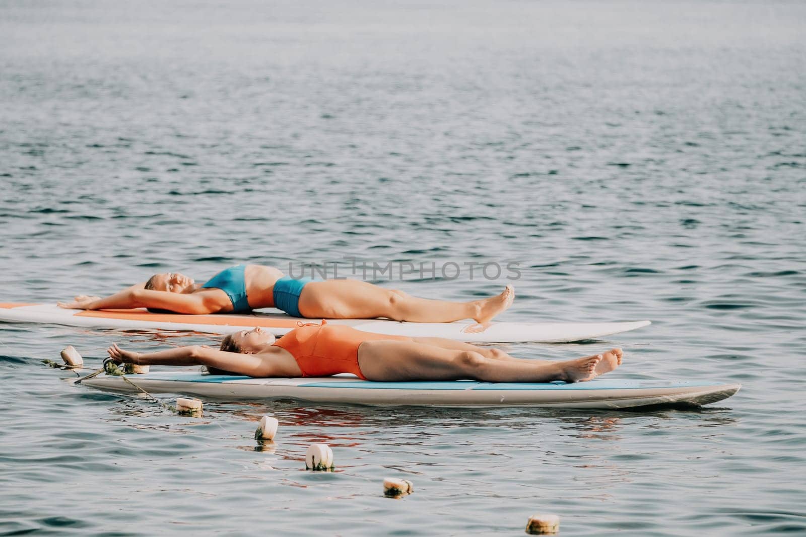 Woman sup yoga. Middle age sporty woman practising yoga pilates on paddle sup surfboard. Female stretching doing workout on sea water. Modern individual hipster outdoor summer sport activity