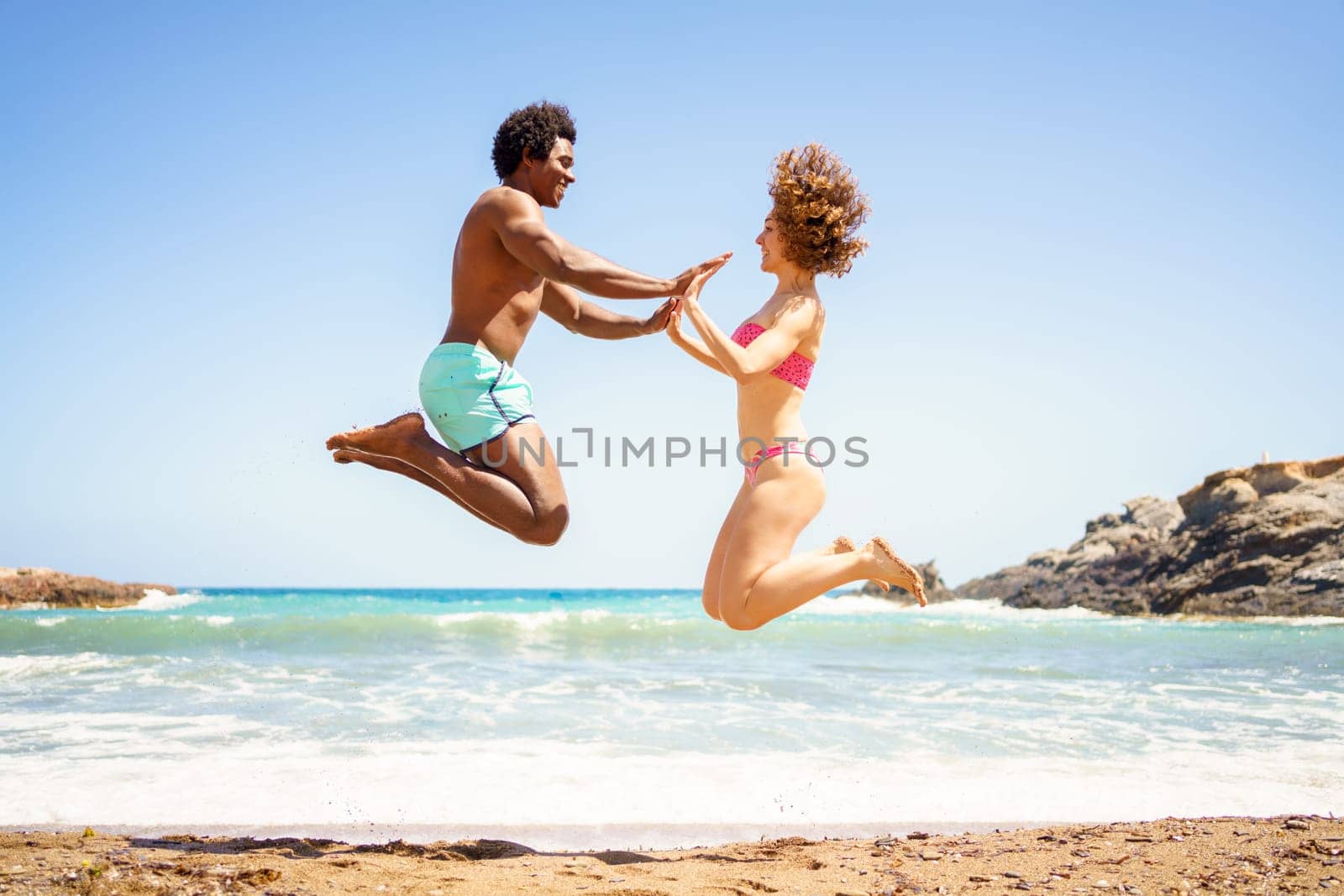 Happy diverse couple jumping near sea by javiindy