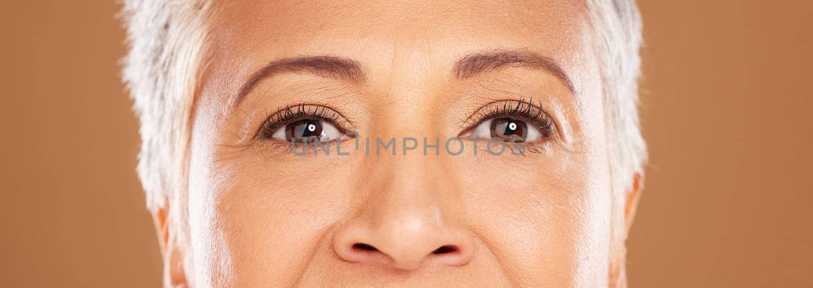 Beauty, eyes and senior woman in studio for skincare, makeup and wellness against a brown background mockup. Face, portrait and elderly woman skin model happy with facial, wrinkles and product result.