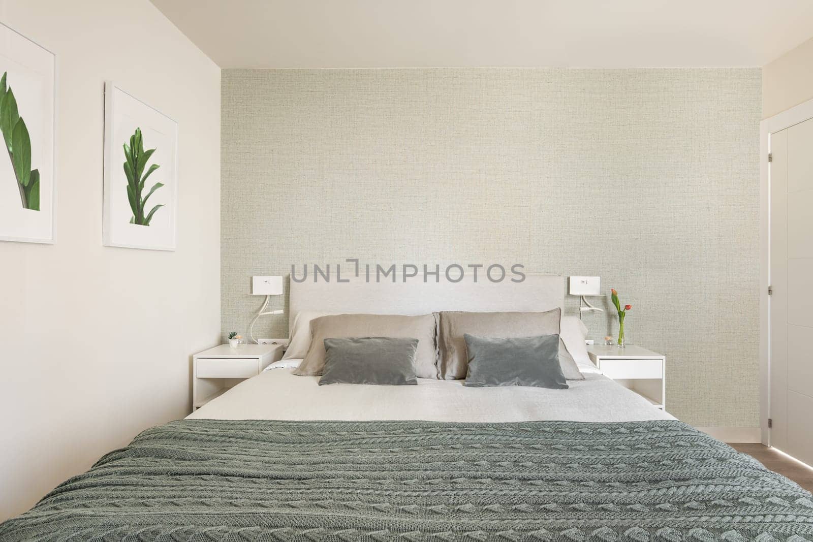 Stylish bright bedroom with bedside tables and a double bed with green beige wallpaper and cute pictures on the wall. The concept of a small but cozy and multifunctional apartment. Copyspace.
