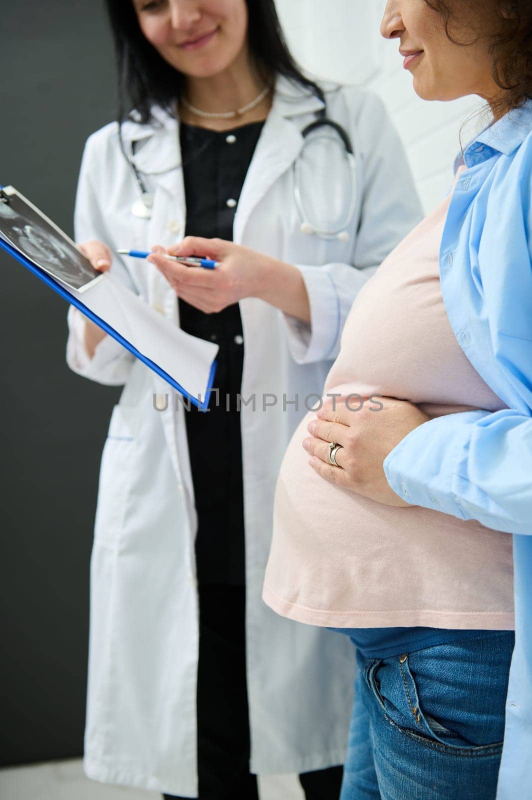 Cropped view pregnant woman holding hand on her big belly while doctor's appointment in obstetric and gynecology clinic by artgf