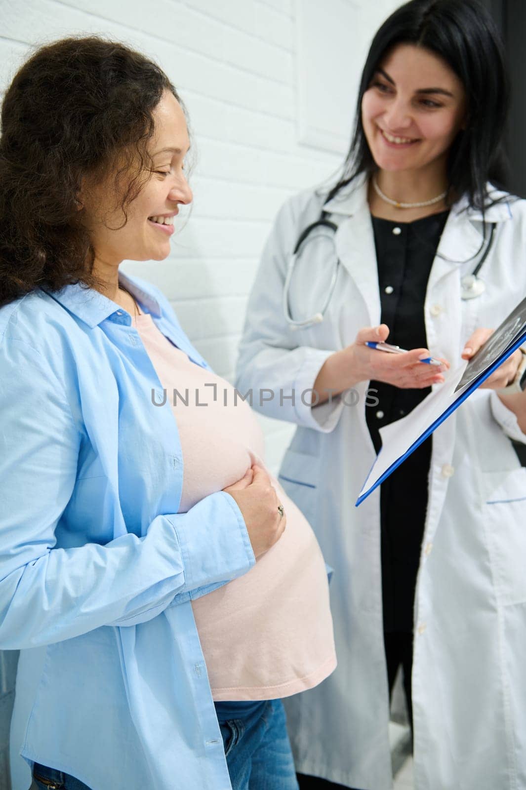 Control ultrasound in 2nd pregnancy trimester of pregnant woman during obstetrician's appointment in maternity clinic. Happy gravid expectant mother expressing positive emotions during medical checkup