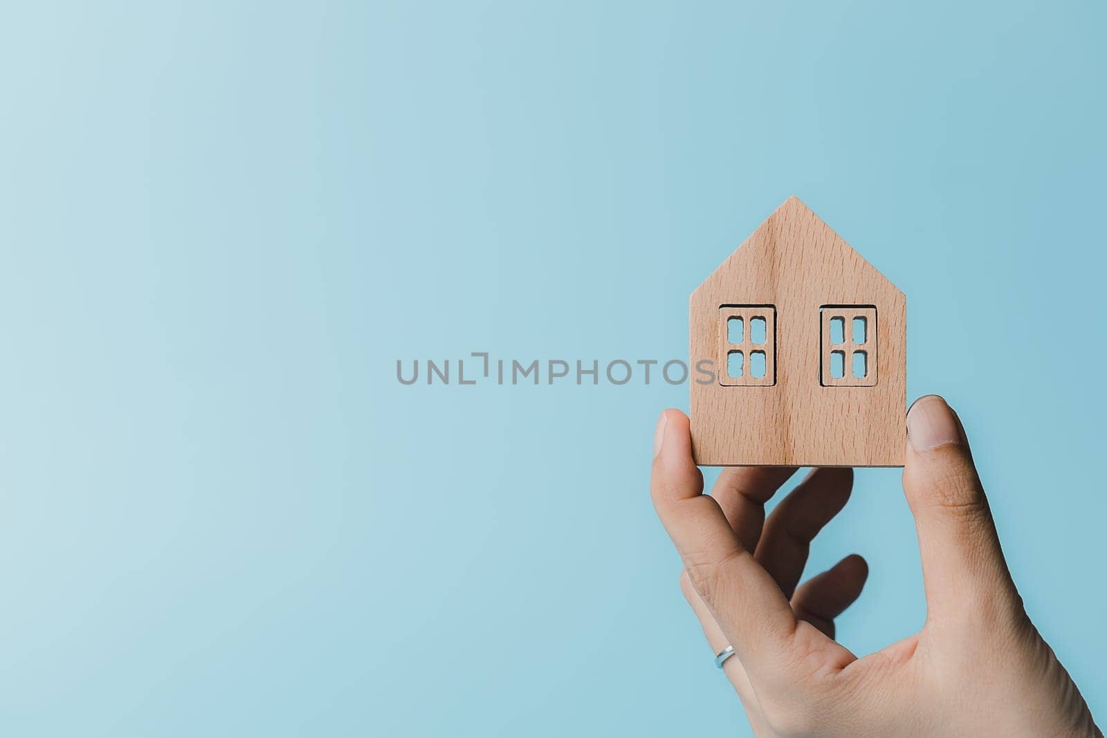 Hand holding a wooden house model on blue background for housing and property concept