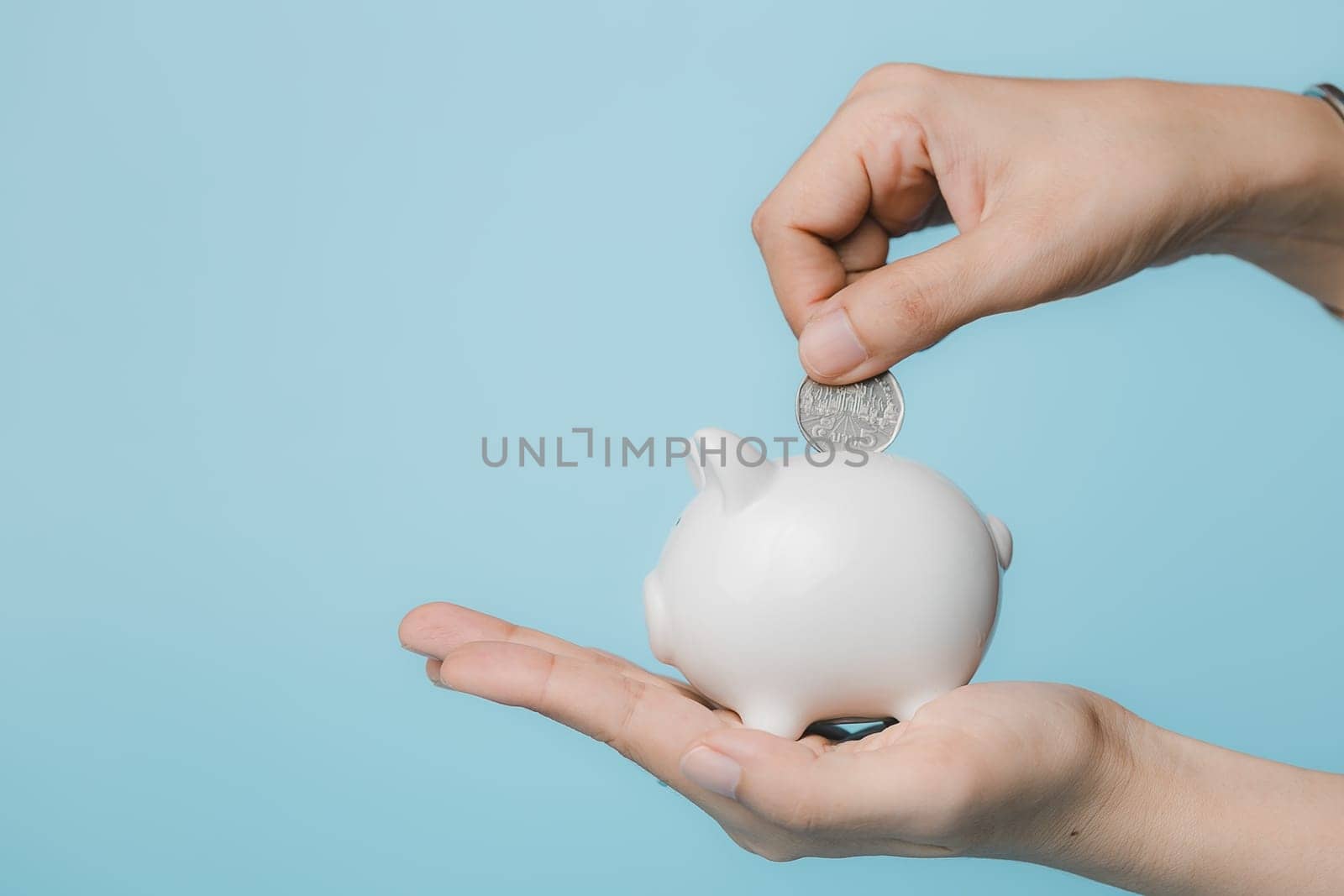 Hand saving a coin into piggy bank  on blue background for investment, business, finance and saving money concept.