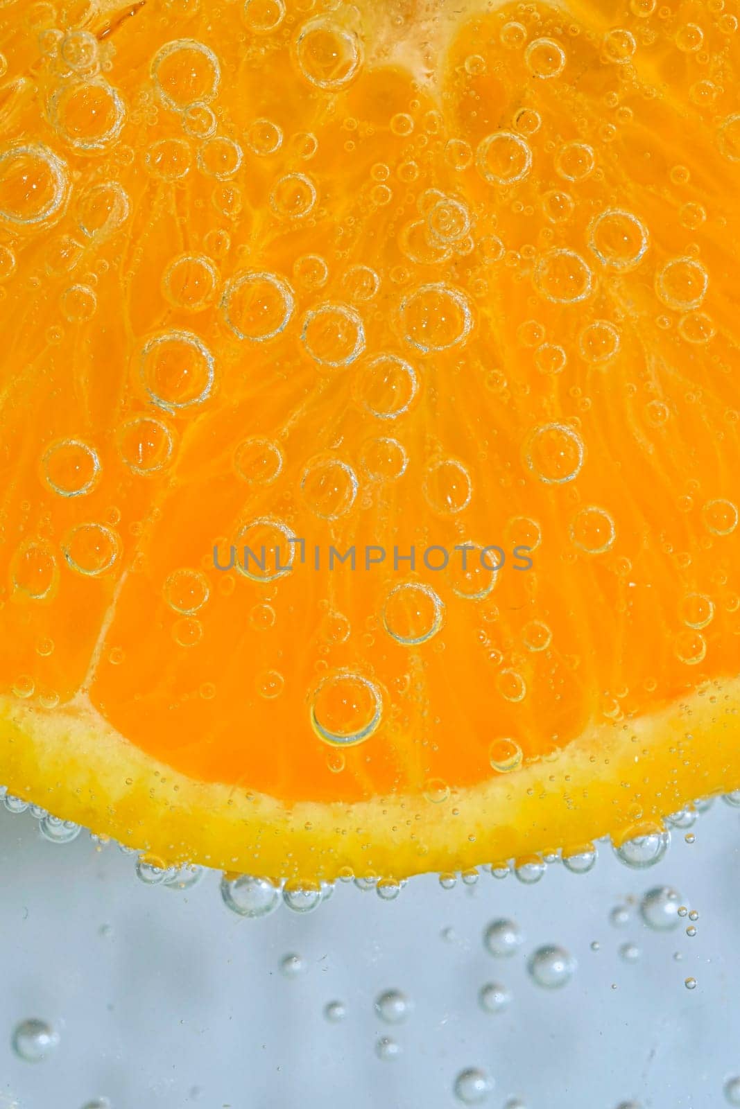 Slice of ripe orange fruit in water on white background. Close-up of orange fruit in liquid with bubbles. Slice of ripe orange fruit in sparkling water. Macro image of fruit in carbonated water