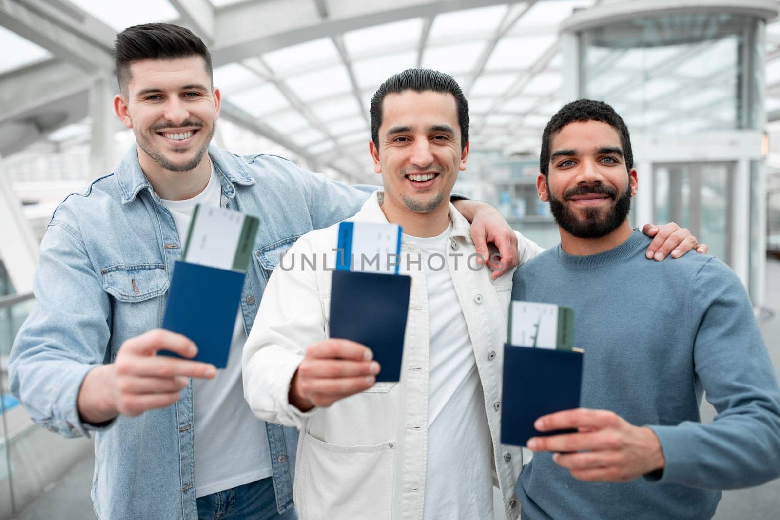 Globetrotters Unite. Three Happy Guys Travelers Embracing At Airport Indoor, Advertising Cheap Tickets Offer Showing Their Passports And Boarding Passes To Camera. Easy Travel And Transportation