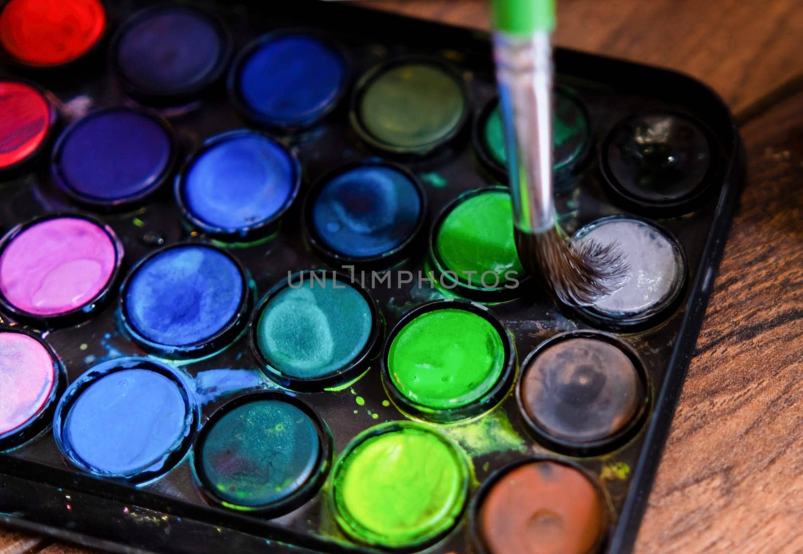 palette of watercolor paints and brushes on a wooden surface.top view