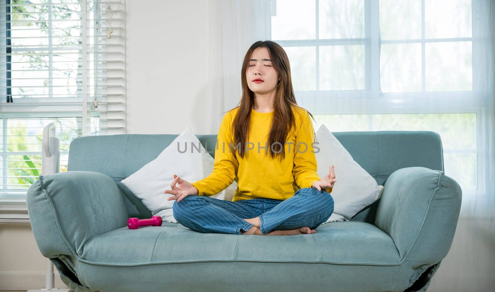 Young woman practise yoga and meditation in lotus position, mindfulness lifestyle, Asian female sits on sofa at home and chilling with couch lotus pose eyes closed, happy relaxation leisure people