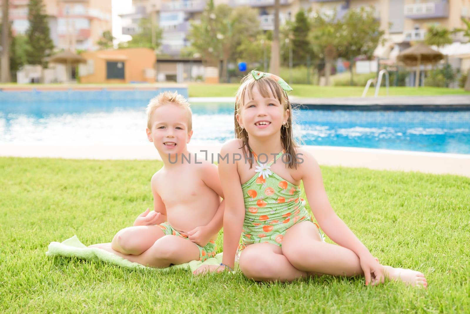 Theme is a children's summer vacation. Two Caucasian children, brother and sister, sit in a perched round pool with water in the yard of the green grass in a bathing suit and joy happiness smile.