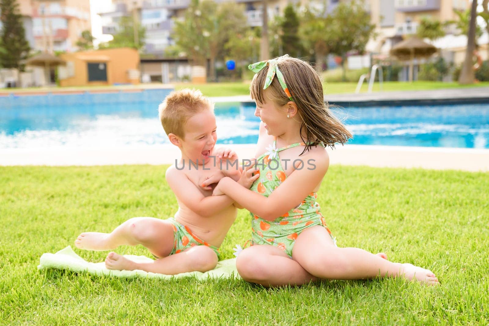 Theme is a children's summer vacation. Two Caucasian children, brother and sister, sit in a perched round pool with water in the yard of the green grass in a bathing suit and joy happiness smile.