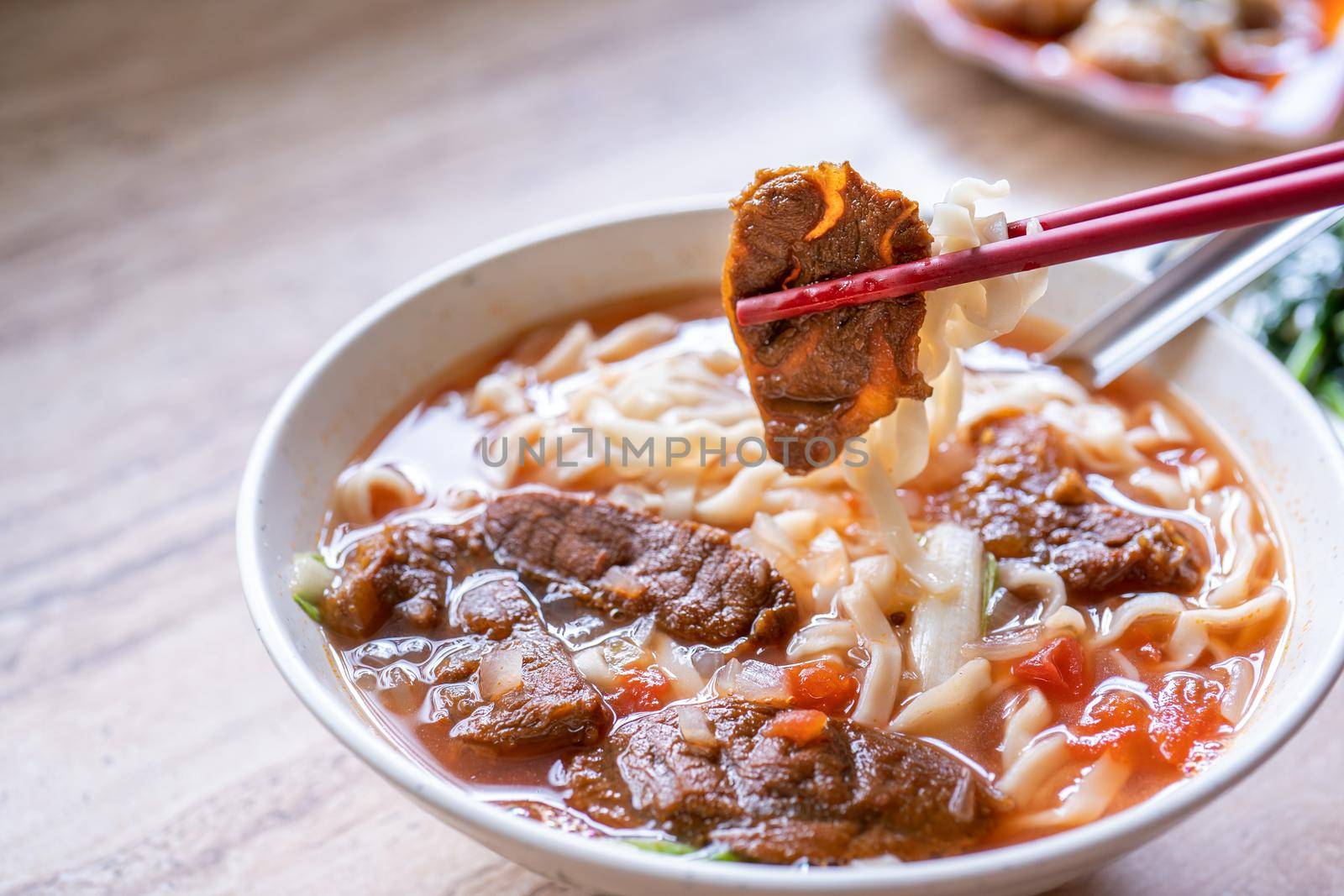 Beef noodle - Taiwan ramen meal with tomato sauce broth in bowl on bright wooden table, famous chinese style food, close up, top view, copy space