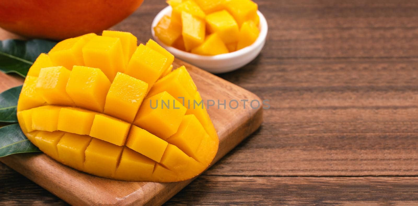 Fresh Mango - Juicy chopped mango cubes on wooden cutting board and rustic timber background. Tropical summer concept. Close up, macro, copy space.  by ROMIXIMAGE