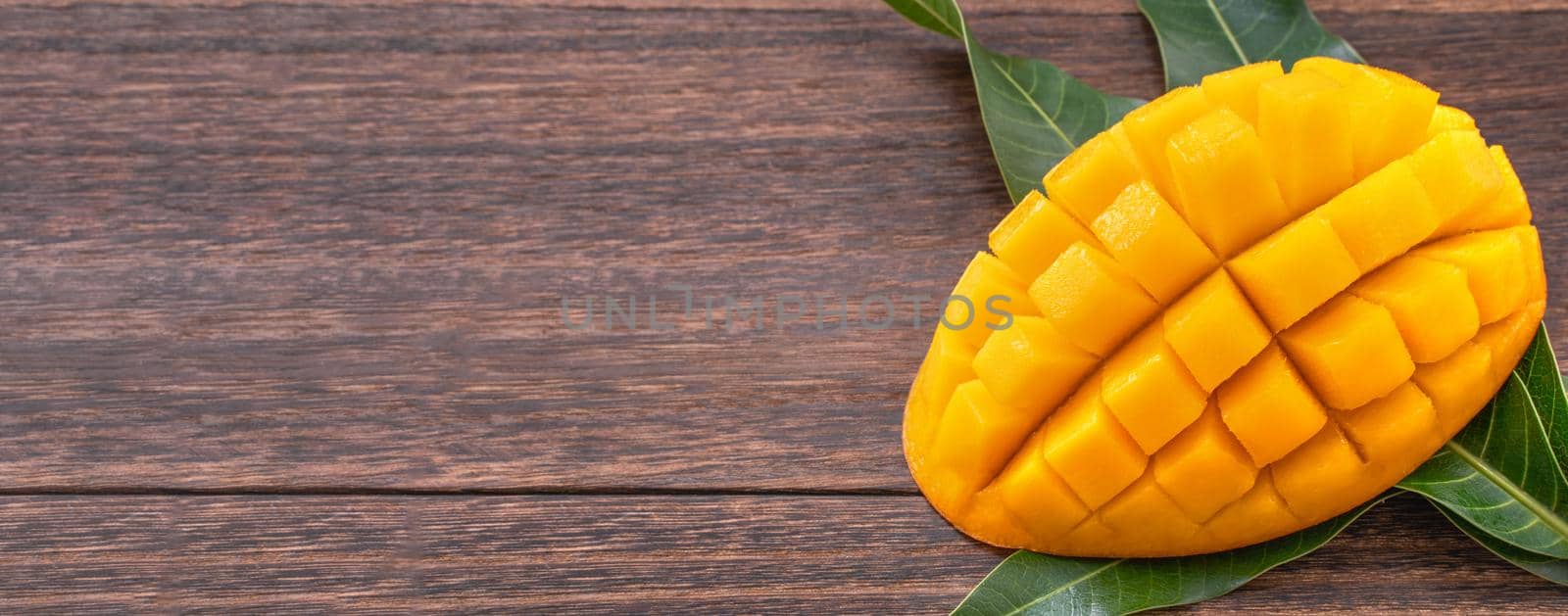 Fresh mango - beautiful chopped fruit with green leaves on dark wood background. Tropical fruit design concept. Flat lay. Top view. Copy space. by ROMIXIMAGE