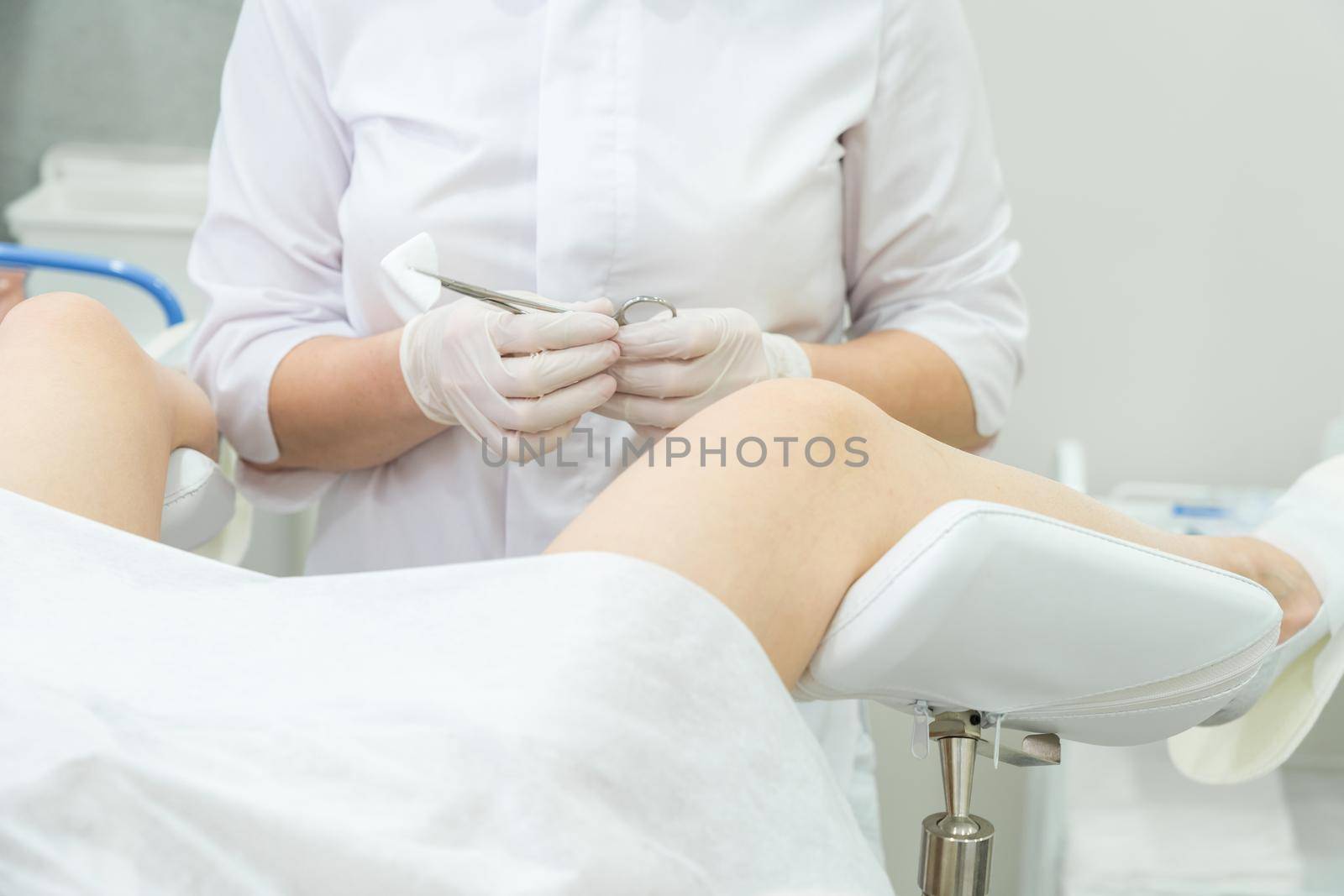 Professional gynecologist examining female patient on gynecological chair holding forceps by Mariakray