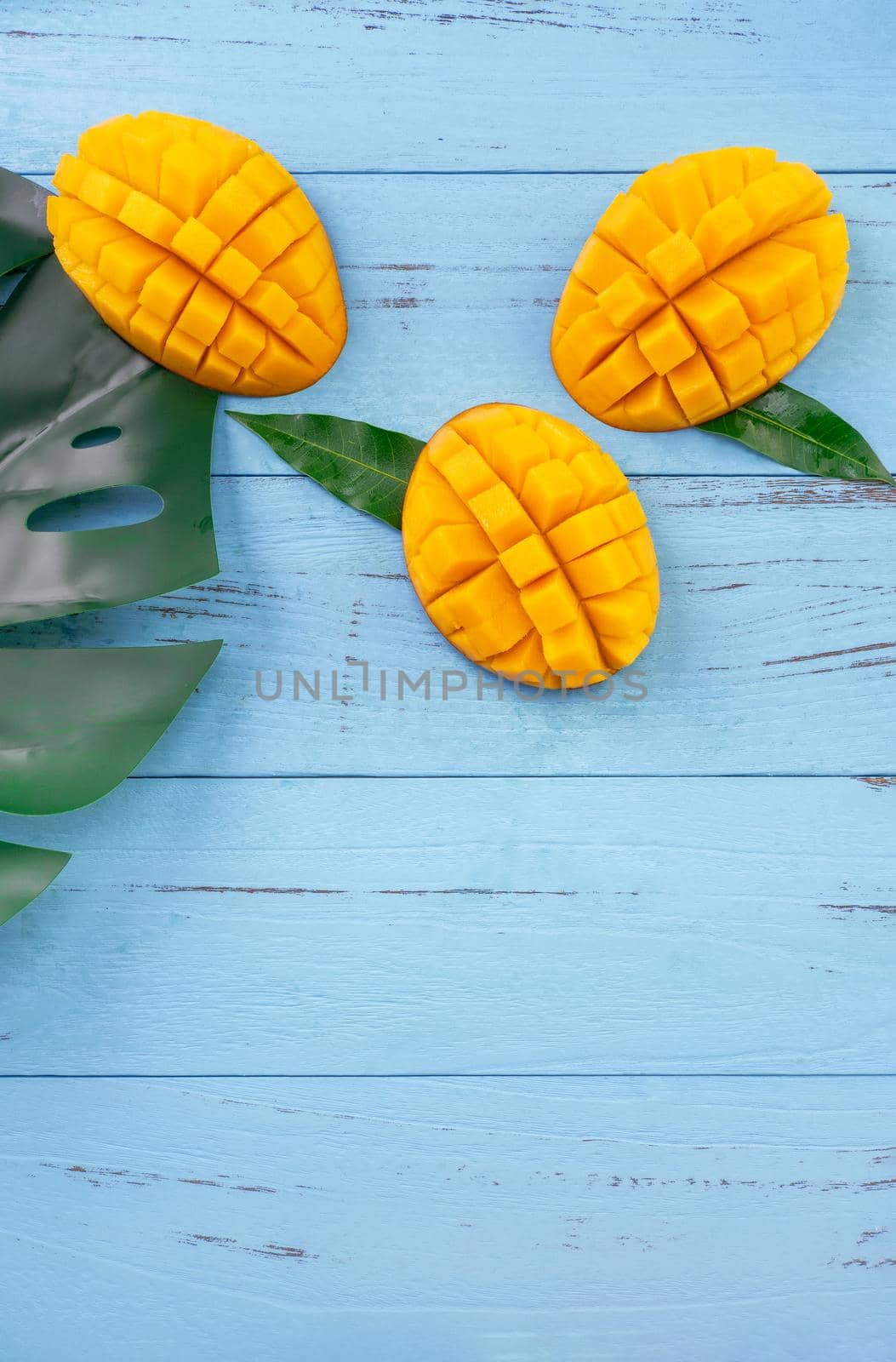 Fresh mango - beautiful chopped fruit with green leaves on bright blue timber background. Tropical fruit design concept. Flat lay. Top view. Copy space