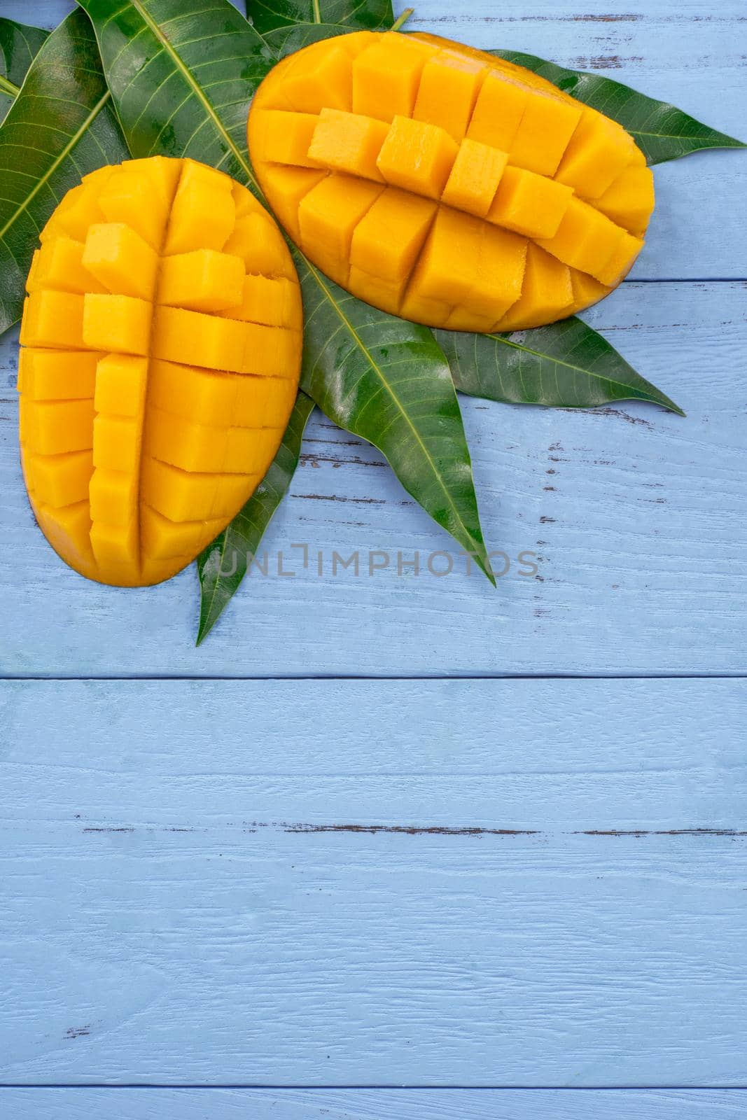 Fresh mango - beautiful chopped fruit with green leaves on bright blue timber background. Tropical fruit design concept. Flat lay. Top view. Copy space by ROMIXIMAGE