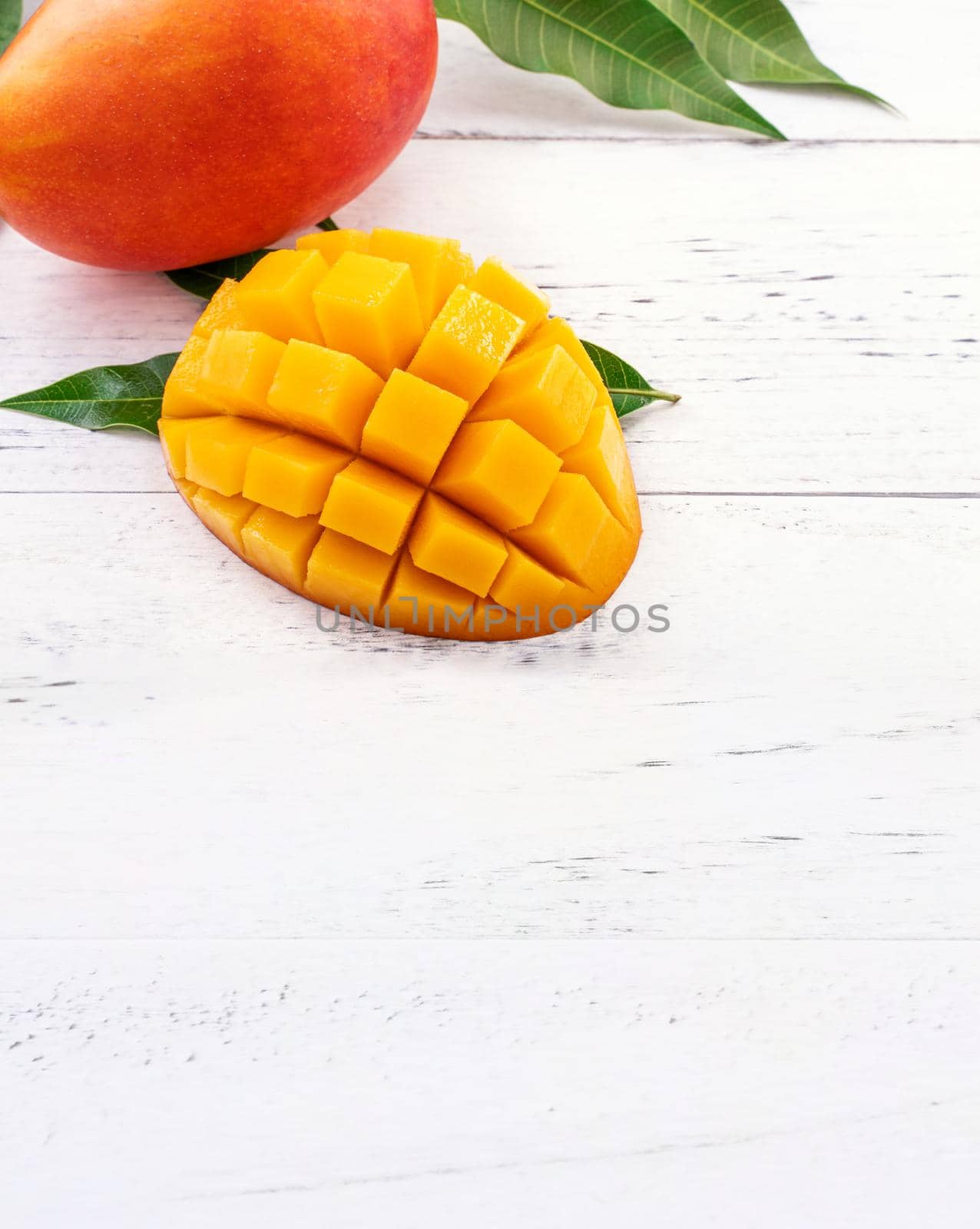 Beautiful chopped mango chunks with green leaves on bright white color timber background. Copy space, close up, macro. Tropical fruit concept. by ROMIXIMAGE