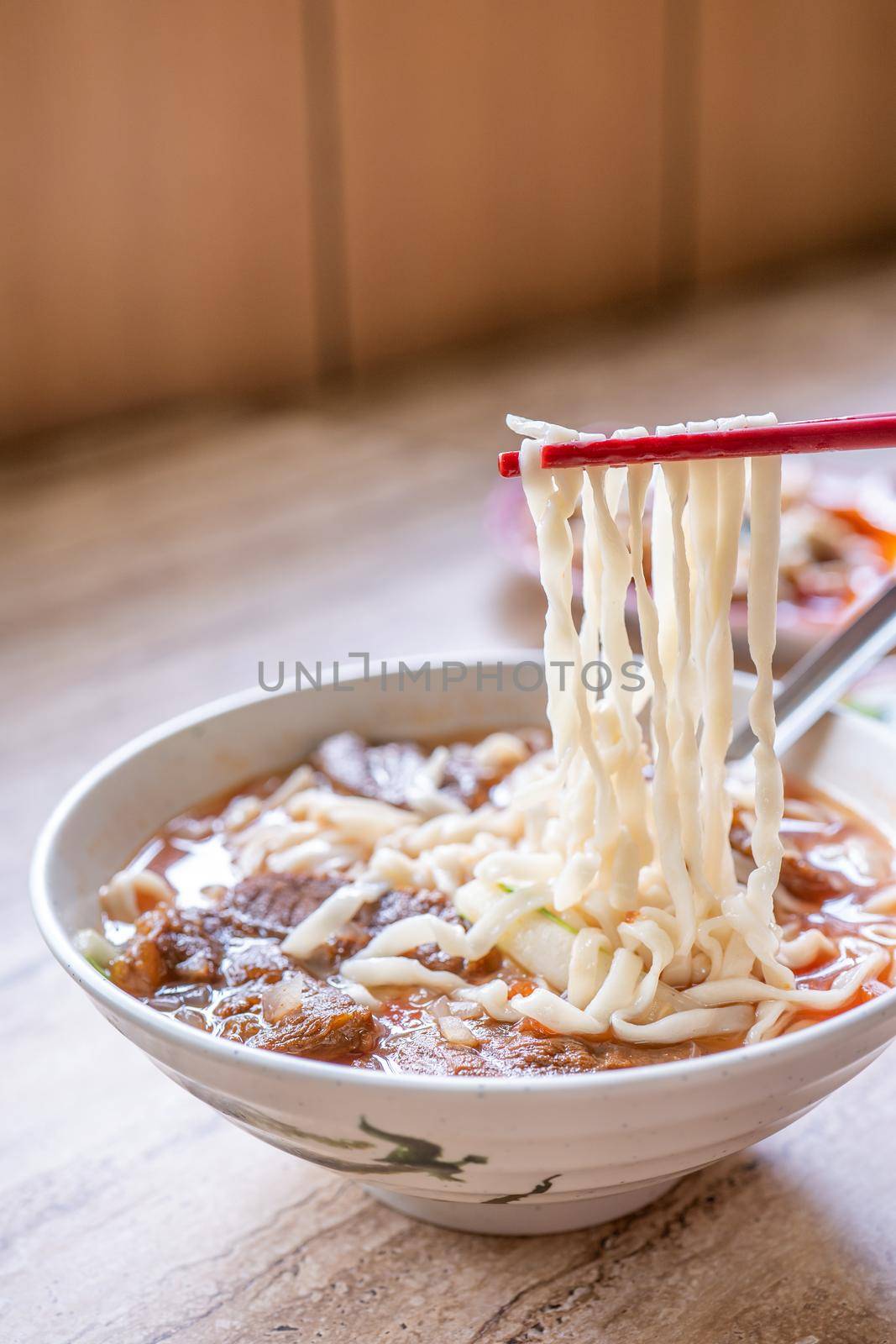 Beef noodle - Taiwan ramen meal with tomato sauce broth in bowl on bright wooden table, famous chinese style food, close up, top view, copy space by ROMIXIMAGE