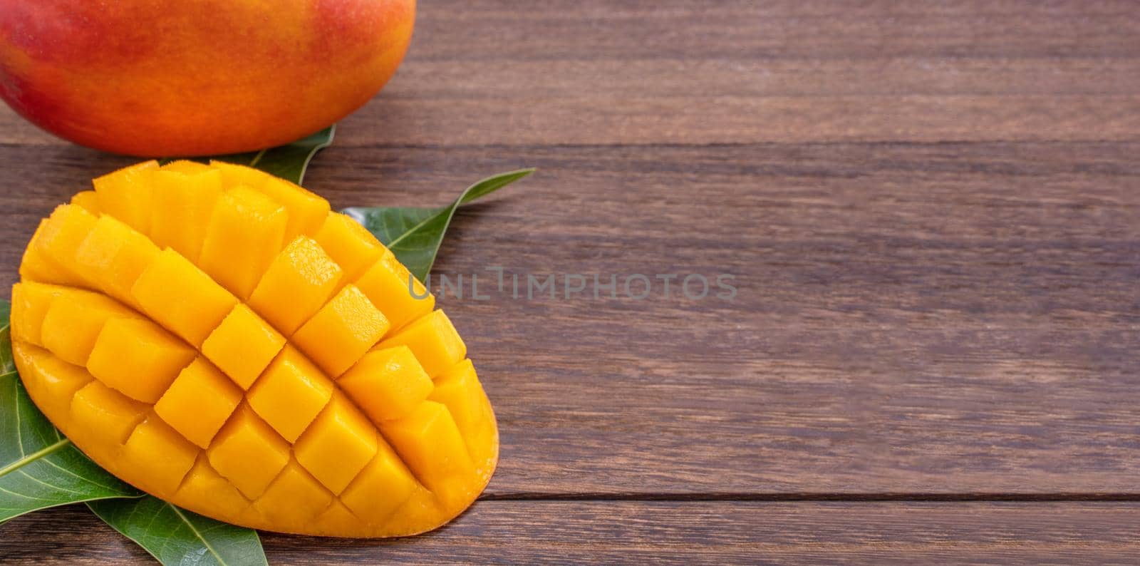 Fresh mango - beautiful chopped fruit with green leaves on dark wood background. Tropical fruit design concept. Flat lay. Top view. Copy space.
